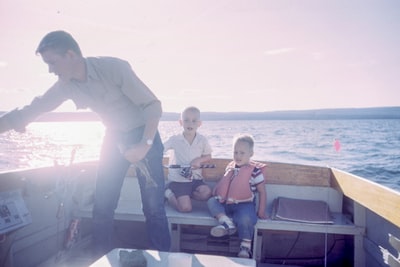 拿着灰色鱼的人站在坐在船座上的两个男孩旁边